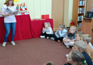Widok na siedzące dzieci, które wsłuchują się w utwór literacki, czytany przez Panią z biblioteki.