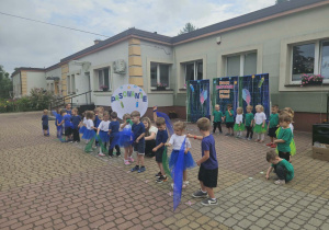 Widok na tańczące dzieci, które poruszają kolorowymi chustkami w rytm muzyki, na tle przygotowanej dekoracji.