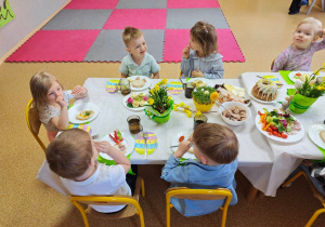 Widok na dzieci siedzące przy pięknie udekorowanym wielkanocnym stole, które wspólnie spożywają przygotowane świąteczne śniadanie.