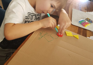 Julek tworzy planszę do gry, odrysowując figury geometryczne na tekturce.