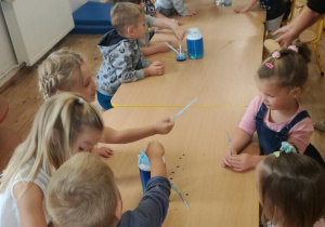 Dzieci siedzą przy stolikach i eksperymentują z niebieskim barwnikiem.