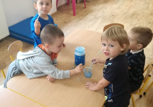 Dzieci siedzą przy stolikach i eksperymentują z niebieskim barwnikiem.