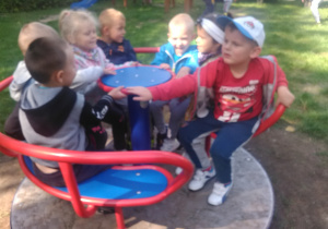 Na placu przedszkolnym grupka dzieci bawi się na karuzeli.