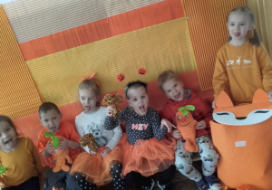 Dzieci w pomarańczowych ubraniach pozują do zdjęcia na pomarańćzowym tle.