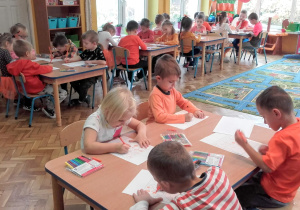 Dzieci siedza przy stolikach i wykonują pracę.