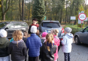 Grupa przedszkolaków z przewodnikiem na parkingu przed wejściem do parku.