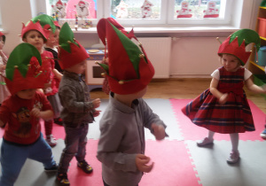 Dzieci w czapkach elfów tańczą przy świątecznej piosence.