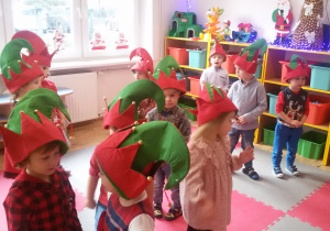 Widok na grupę dzieci w czapkach elfów, które stoją na dywanie i śpiewają świąteczną piosenkę.