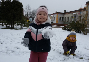 Widok na zaśnieżony ogród przedszkolny i bawiące się na śniegu dzieci.