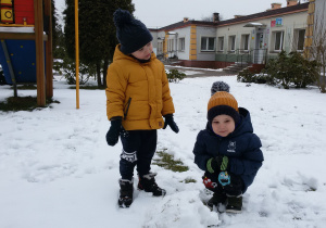 Widok na zaśnieżony ogród przedszkolny i bawiące się na śniegu dzieci.