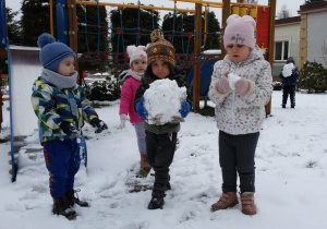 Widok na zaśnieżony ogród przedszkolny i dzieci, które trzymają w rękach śnieżne kule.