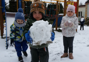 Widok na zaśnieżony ogród przedszkolny i dzieci prezentujące swoje kule śniegowe.