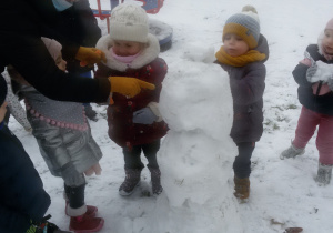 Widok na zaśnieżony ogród przedszkolny i dzieci, które bawią się na śniegu.