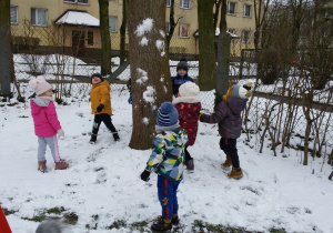 Widok na zaśnieżony ogród przedszkolny i rzucające śnieżkami dzieci.