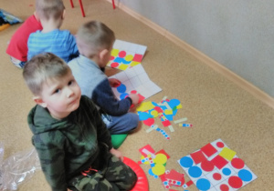 Chłopcy siedząc na podłodze układają figury geometryczne (koło, kwadrat) wg kodu