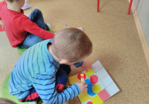 Chłopcy siedząc na podłodze układają figury geometryczne (koło, kwadrat) wg kodu