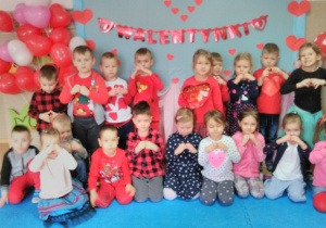 Dzieci pozują do zdjęcia grupowego na tle dekoracji walentynkowej. Z dłoni tworzą kształt serca.