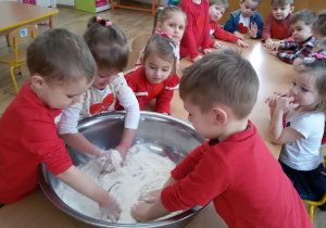 Maluszki w dużej metalowej misce mieszają rękami mąkę z solą.