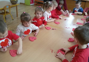 Widok na dzieci, które siedzą przy długim stole i lepią serduszka z czerwonej masy solnej.