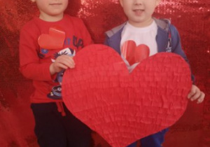 Olek i Fabian pozują do zdjęcia trzymając w rękach duże czerwone serce.