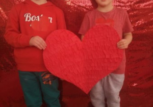 Jakub i Leoś pozują do zdjęcia trzymając w rękach papierowe, czerwone serce.