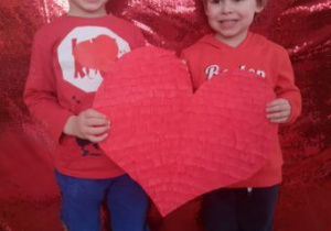 Dwóch chłopcy pozuje do zdjęcia trzymając w rękach czerwone serce.