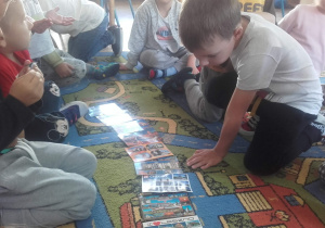 Dzieci oglądają kartki pocztowe z różnych miejscowośći.