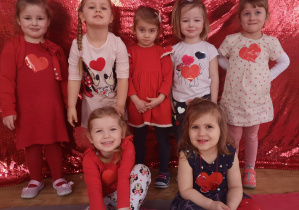 Grupa dziewczynek pozuje do zdjęcia na czerwonym tle.
