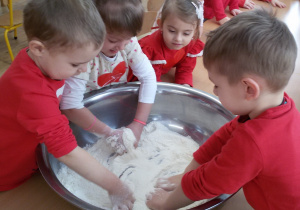 Widok na dzieci, które mieszają rączkami w dużej metalowej misce mąkę z solą.