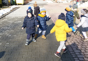 Widok na plac przed przedszkolem i grupę bawiących się dzieci.