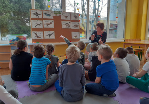 Nauczycielka czyta zagadki o dinozaurach. dzieci siedzą przed tablicą