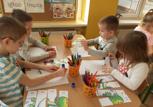 Dzieci układają rozcięte puzzle z dinozaurów. Praca przy stolikach