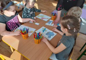Dzieci układają rozcięte puzzle z dinozaurów. Praca przy stolikach