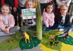 Dzieci pozują do zdjęcia. przed dziećmi jest zrobiona mini dżungla z czasów dinozarów