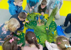 Dzieci bawią się dinozaurami w przygotowanej przez nauczycielką prehistorycznej dżungli