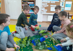 Dzieci bawią się dinozaurami w przygotowanej przez nauczycielką prehistorycznej dżungli