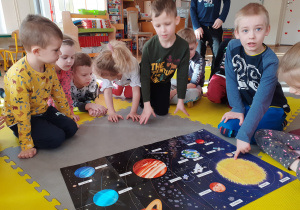 Dzieci obserwują plakat i odczytują napisy dotyczące kosmosu.