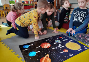 Dzieci obserwują plakat i odczytują napisy dotyczące kosmosu.