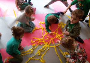 Widok na dzieci, które układają na dywanie wokół żółtej obręczy, bibułkowe promyki.