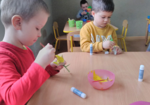 Dzieci siedząc przy stoliku malują żółtą farbą kielich tulipana wyciętego z tekturki.