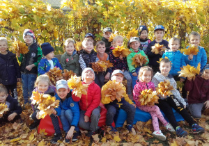 Duża grupa dzieci trzyma liście i pozuje do zdjęcia.