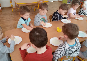 Widok na dzieci siedzące przy stoliku i malujące farbami na mleku.
