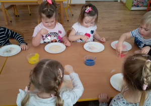 Widok na dzieci siedzące przy stoliku i malujące farbami na mleku.