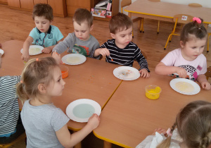 Widok na dzieci, które siedzą przy stole i malują farbami na mleku.