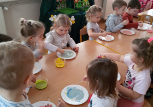Widok na grupę dzieci, które tworzą barwne kompozycje na mleku.