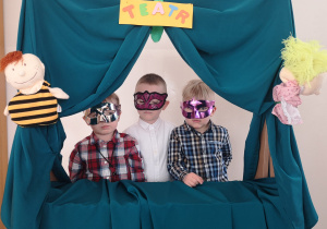 Widok na trzech chłopców w maskach, którzy stoją w oknie teatrzyku przedszkolnego.