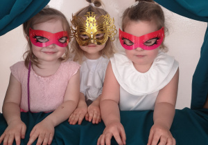 Widok na trzy dziewczynki w maskach karnawałowo- teatralnych.