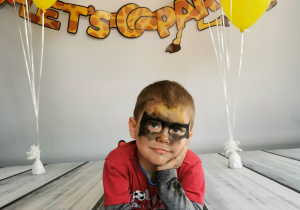 Chłopiec leży na tle fotograficznym i pozuje do zdjęcia wśród balonów.