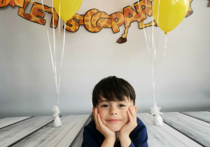 Chłopiec leży na tle fotograficznym i pozuje do zdjęcia wśród balonów.