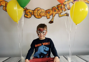 Chłopiec siedzi na tle fotograficznym i pozuje do zdjęcia wśród balonów